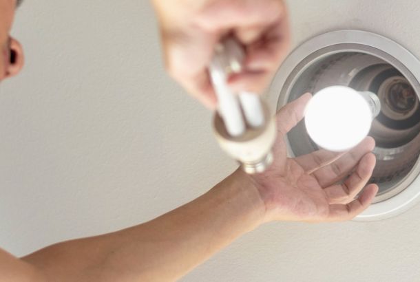 Power saving concept. Hands holding new Light Emitting Diode ( LED ) light bulb with light on and blur spiral compact-fluorescent (CFL) bulbs behind for copyspace.